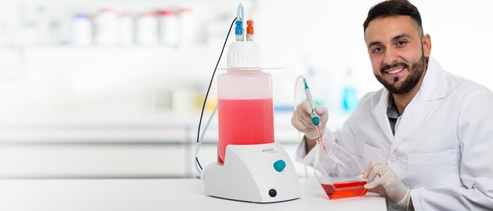 Scientist using a VACUSAFE aspiration system to aspirate red liquid from a cell culture flask