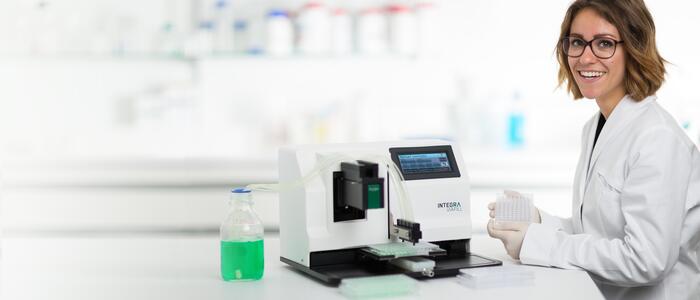 Scientist holding a well plate next to a VIAFILL microplate dispenser.