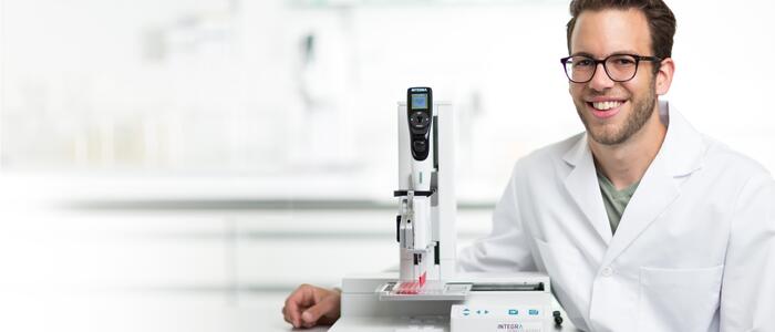 Scientist smiling, with ASSIST automated pipetting system next to him..
