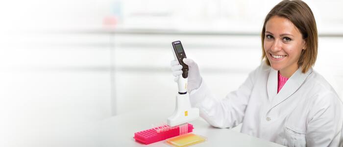 Scientist using a VOYAGER adjustable tip spacing pipette to transfer liquid from Eppendorf tubes to 96 well plate.