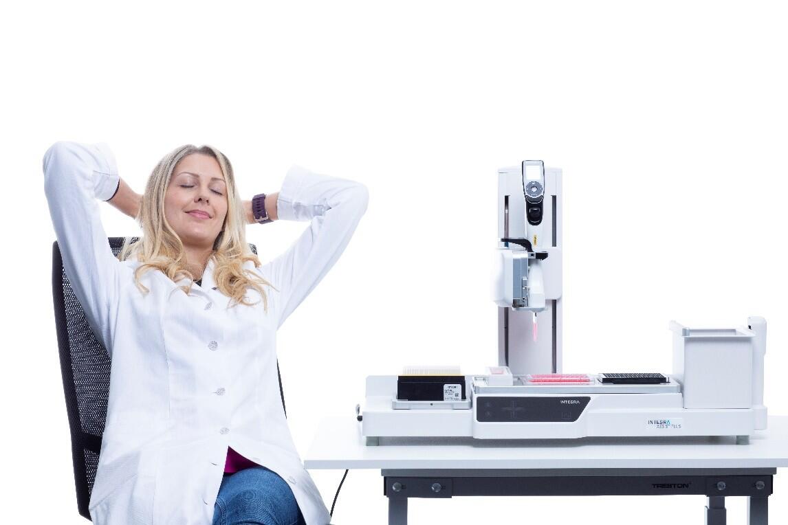 Scientist relaxing on a chair next to an ASSIST PLUS pipetting robot doing the work for her