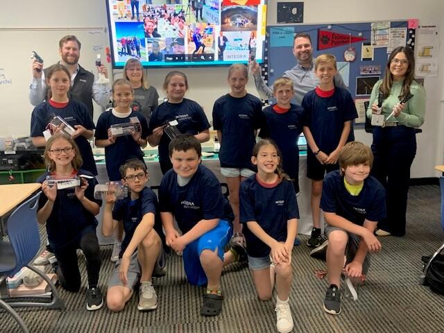 A group of elementary school students and INTEGRA Biosciences employees posing with INTEGRA pipettes and merchandise