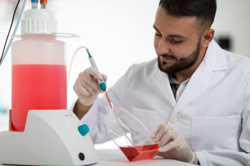 Scientist using VACUBOY vacuum hand operator and VACUSAFE vacuum system to aspirate red liquid from T-Flask