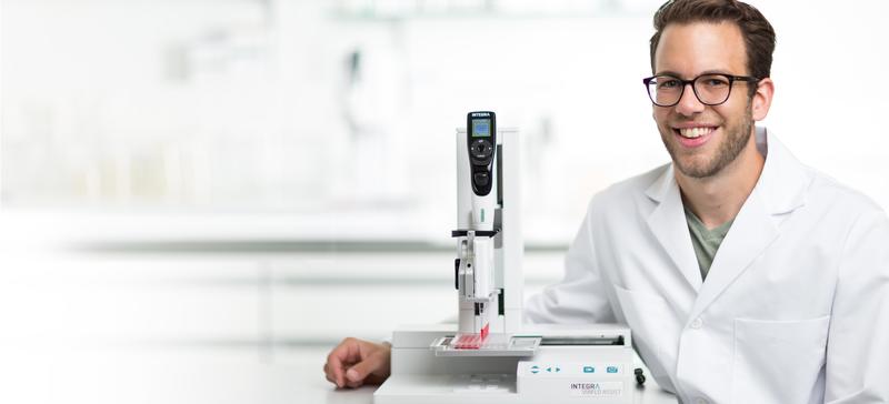 Scientist smiling, with ASSIST automated pipetting system next to him..