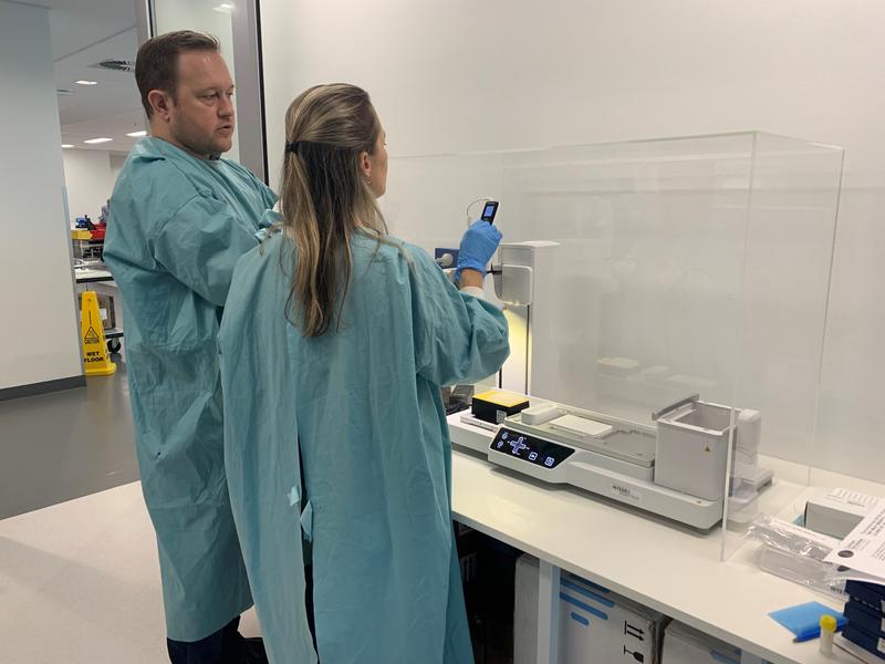 Two scientists standing in front of the ASSIST PLUS pipetting robot used to test patient samples for COVID-19