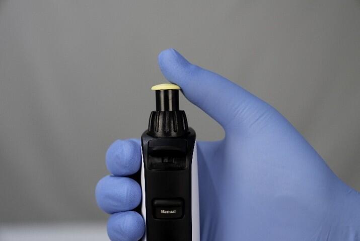 Nahaufnahme der Hand eines Forschenden, die eine SWITCH-Pipette hält, wobei der Daumen auf dem Kolben ruht.